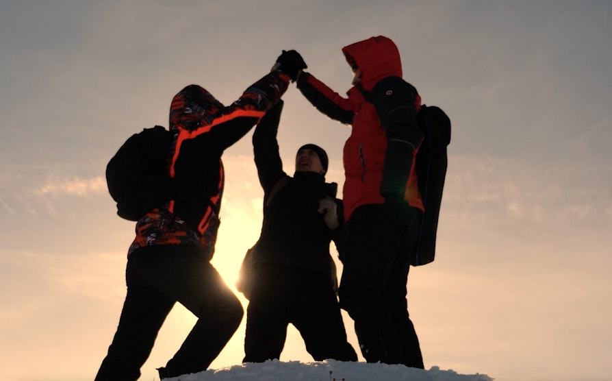 Tre personer ute i snøen som tar en high five. Brukt til Grasrot
