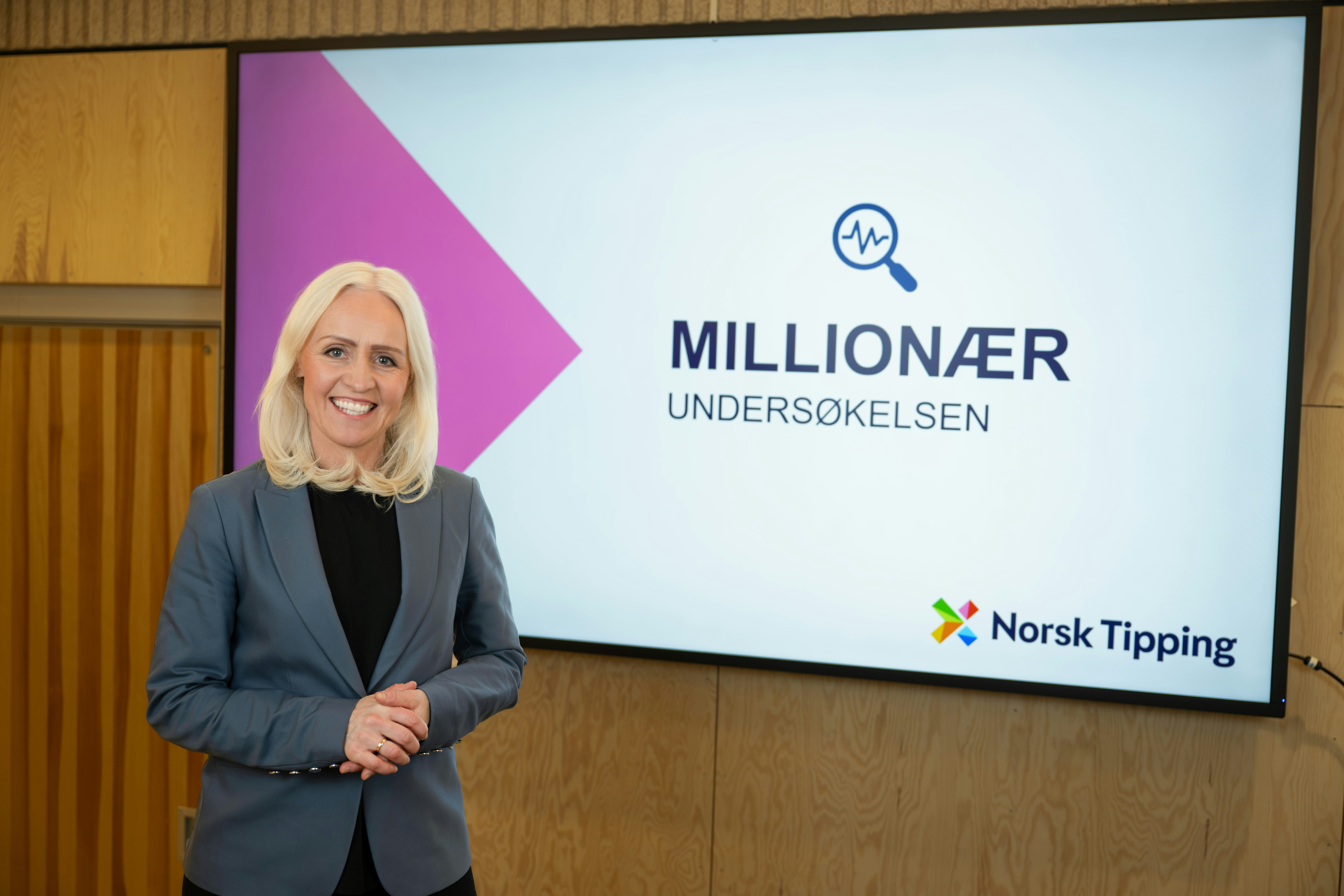 Bilde av lotteri- og trekningsansvarlig Ingrid Roterud Mathisen i Norsk Tipping. Bilde i forbindelse med Millionærundersøkelsen 2025. Står foran lerret med Millionærundersøkelsen-grafikk. Innendørs.