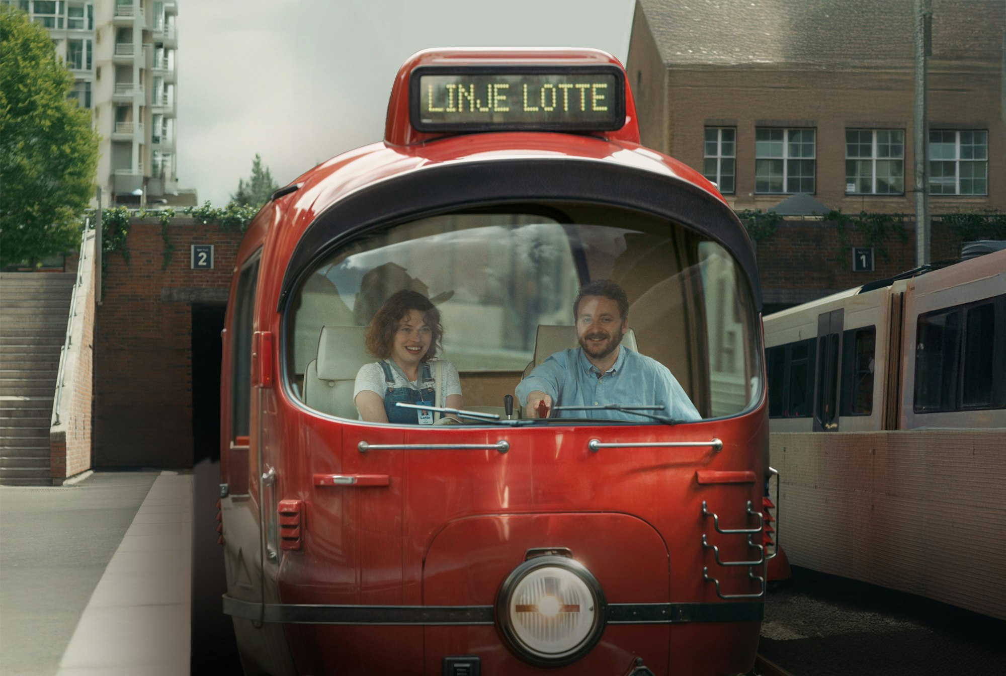 Foto fra reklamefilmen Linje Lotte. Lotte og Truls i førerkupeen på et rødt veterantog.