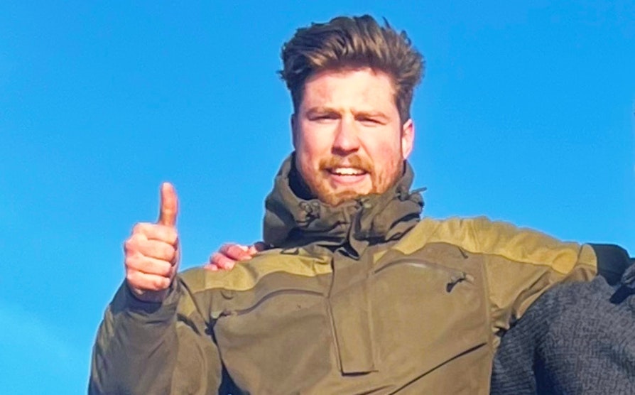 Portrett av Supertrekning-vinner Joakim Klingenberg Norberg med rødlig blondt hår og skjegg og grønn hettejakke som holder tommelen opp og smiler med blå himmel i bakgrunn.