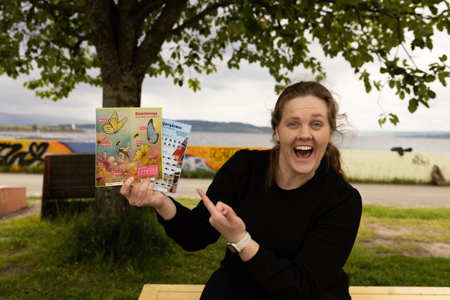 Smilende kvinne holder opp to Flax Sommer-hefter. Grønt og sommerlig rundt.