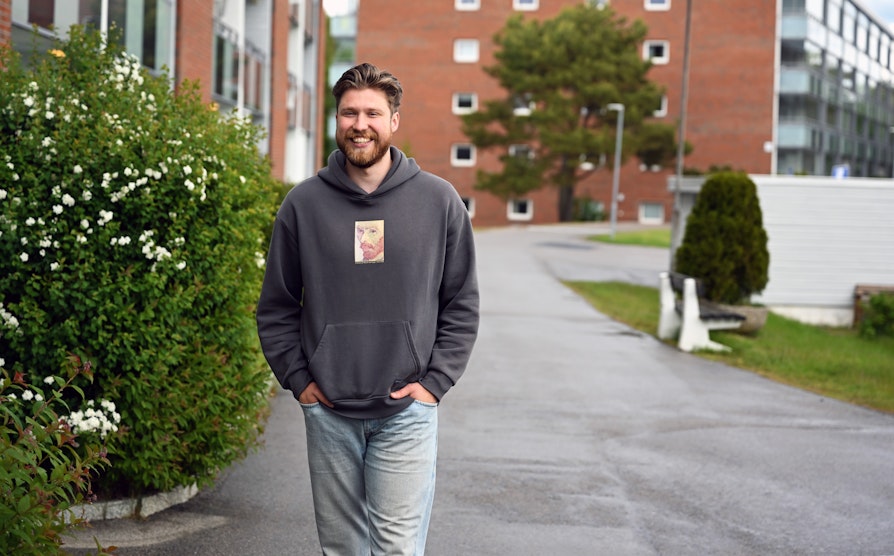 Superttrekning-vinner Joakim Nordberg Klingenberg, smilende med rødlig skjegg, grå hettegenser og jeans, går foran boligblokken han bor i.