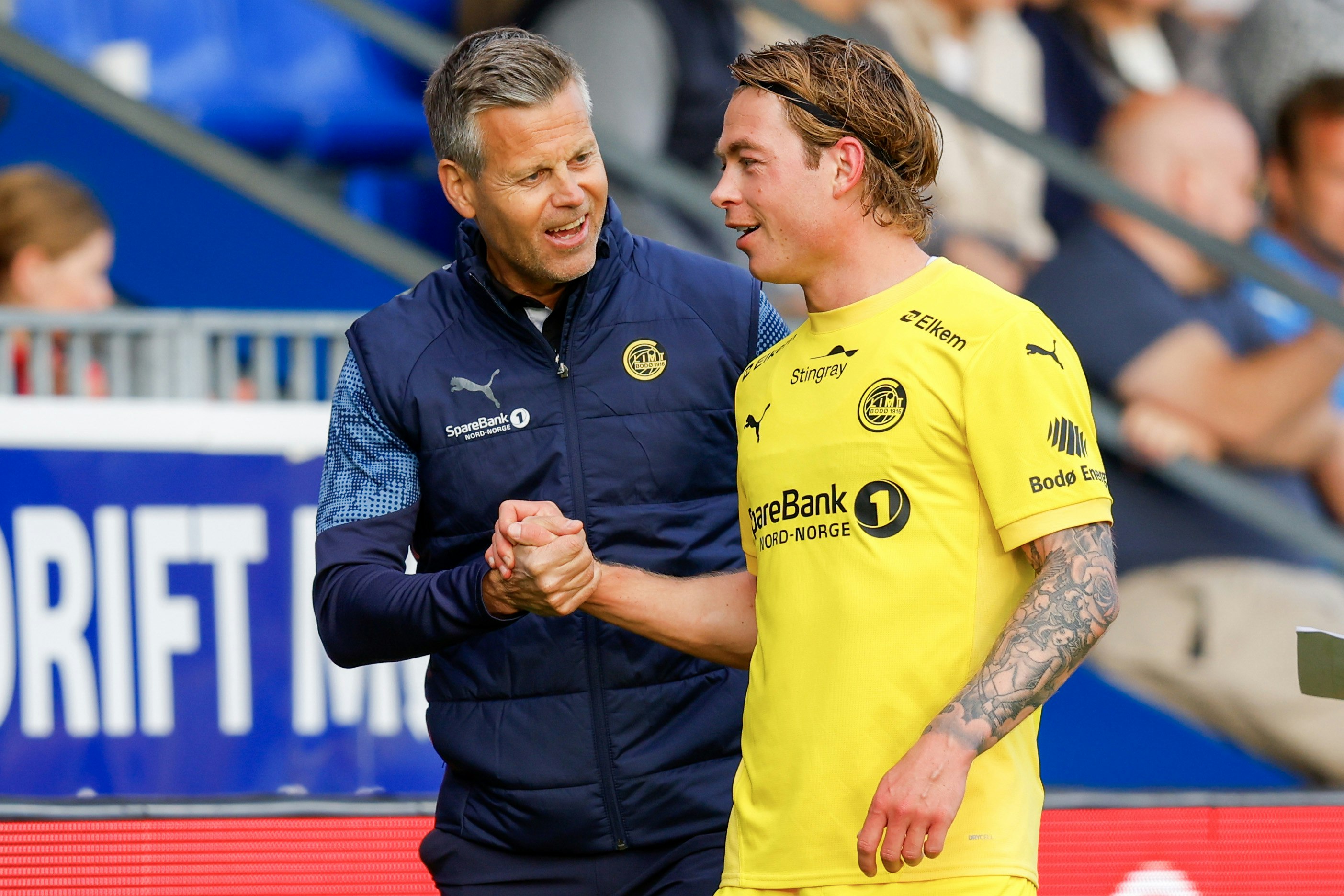 Bodø/Glimt-trener Kjetil Knutsen og midtbanestrateg Patrick Berg avbildet sammen etter en kamp mot Kristiansund. Tar hverandre i hendene og ser fornøyde ut.
