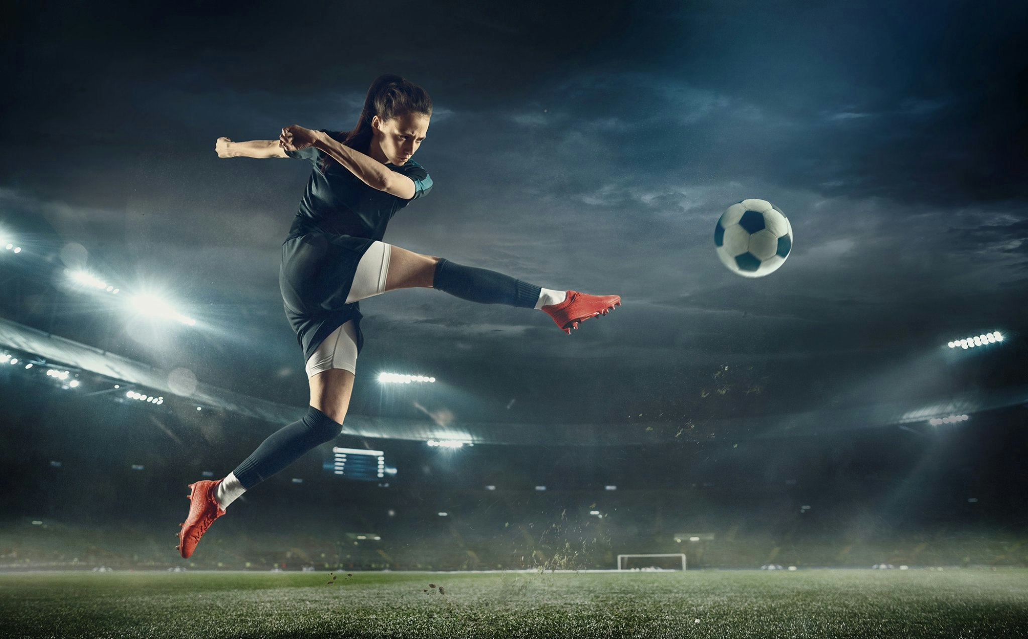 Kvinne sparker en fotball ute på en fotballbane.