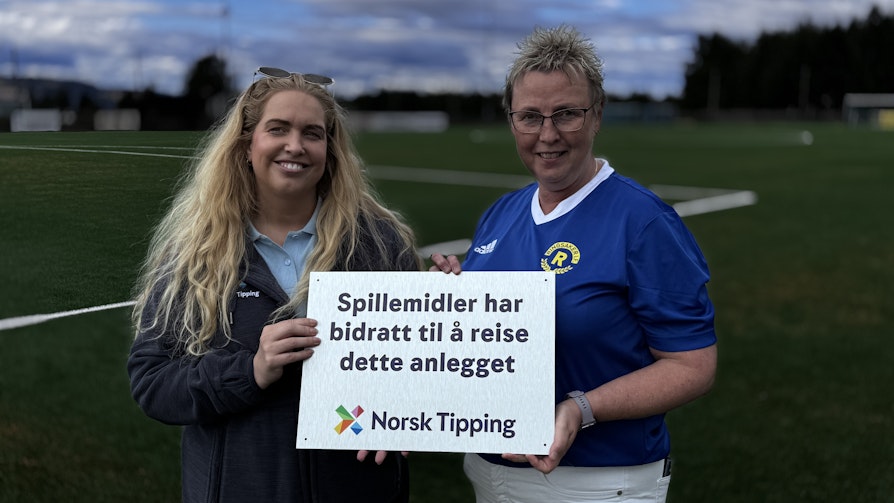 Kristing Pålsrud og Inger Amb holder i et skilt hvor det står: Spillemidler har bidratt til å reise dette anlegget. Og nederst har det logoen til Norsk Tipping.