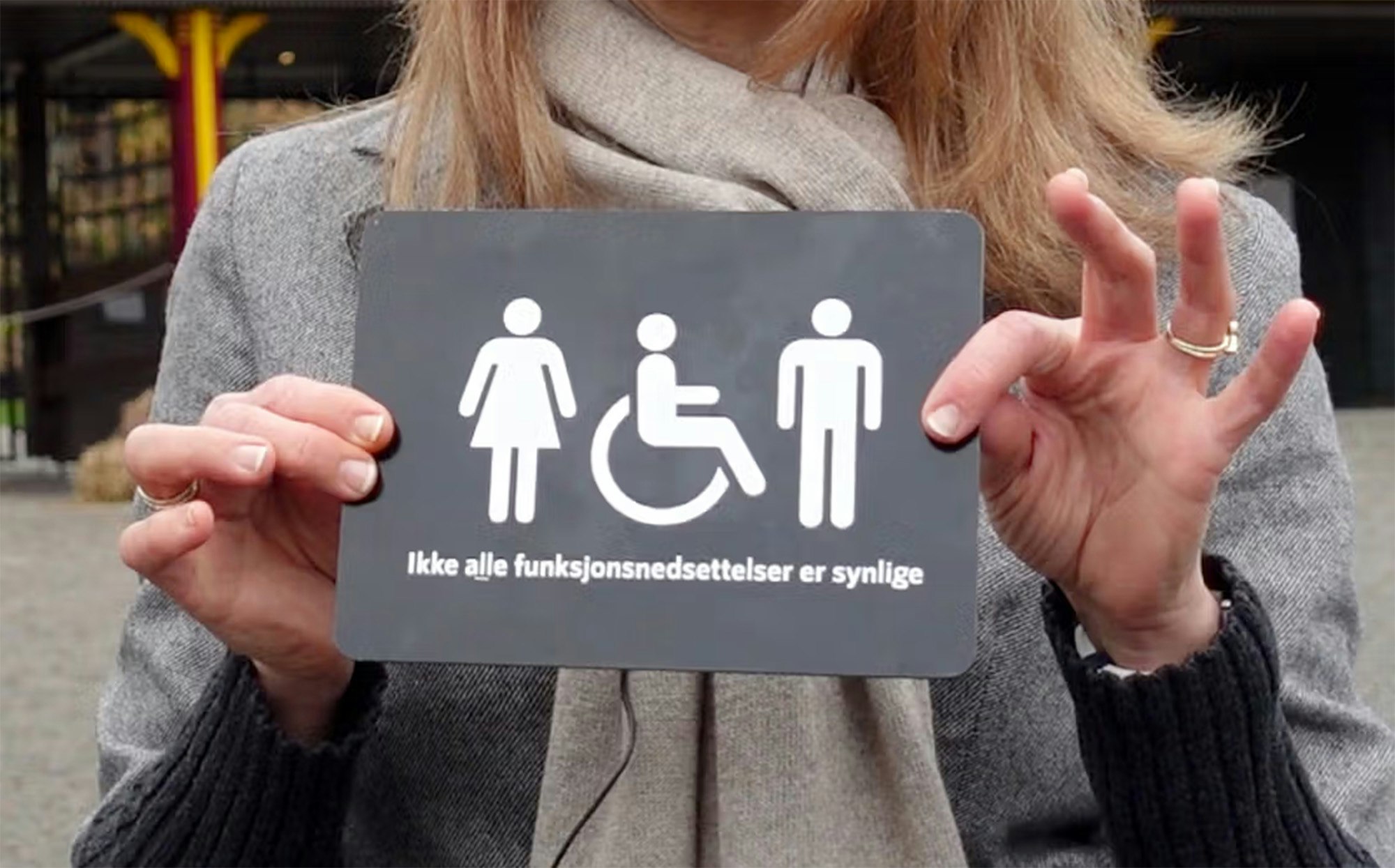 Kvinne holder opp skiltet for kampanjen "Ikke alle funksjonsnedsettelser er synlige".