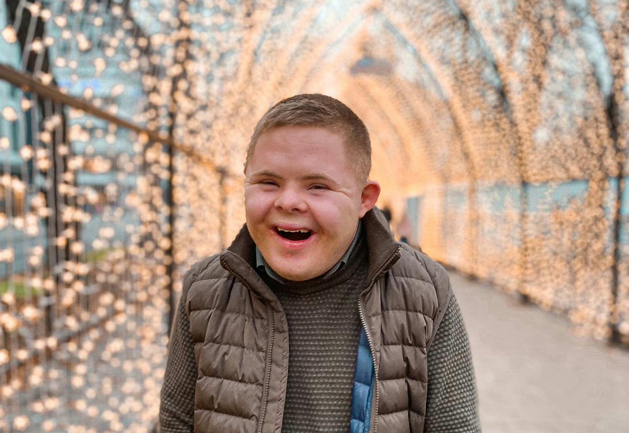 Sondre har Down syndrom. Han står i en tunnel av julelys, ser inn i kamera og er veldig glad.