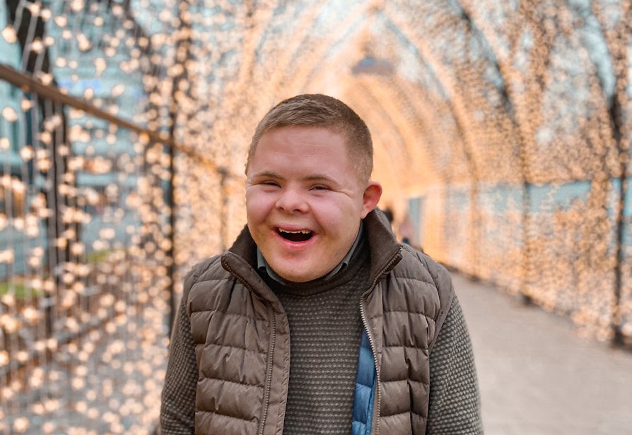 Sondre har Down syndrom. Han står i en tunnel av julelys, ser inn i kamera og er veldig glad.