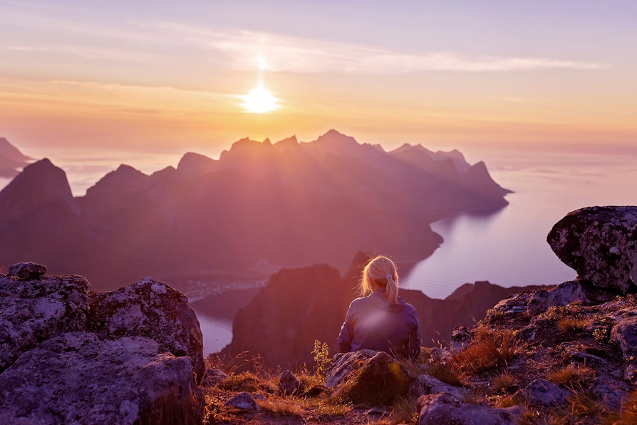 Kvinne sitter i fjellandskap og ser utover vannet og på solnedgangen. Lilla farger i bildet, da det er brukt i en vinnersak for Extra.