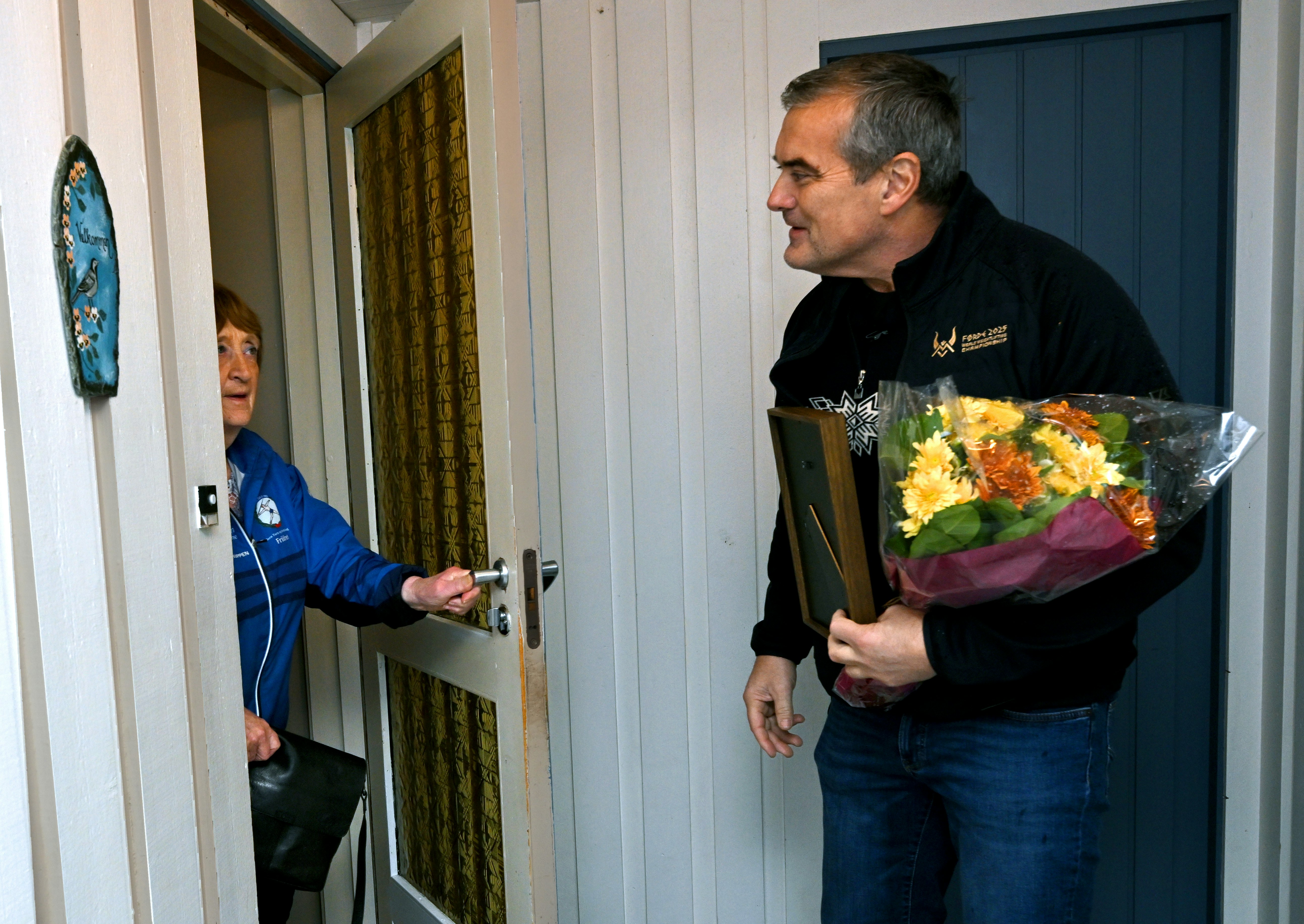 Annbjørg Sunnarvik, Florø turn- og idrettsforening, er Vestlands kretsvinner til illdsjelprisen 2026. Hun er én av 12 kretsvinnere som møter til Idrettsgallaen på Hamar 10. januar. Mandag 17. nov. 2025 ble hun overrasket av Norsk Tipping og Norges idrettsforbund hjemme i Florø. Her fotografert ved inngangsdøra hjemme i Florø. Den gamle vektløfteren Stian Grimseth overrasker med diplom og blomster. orset, Norsk Tipping)