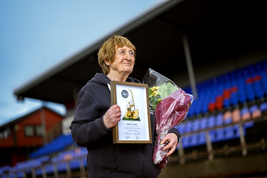 Bilde av Annbgjørg Sunnarvik på Florø stadion. Holder diplom og blomster stående foran tribunen.