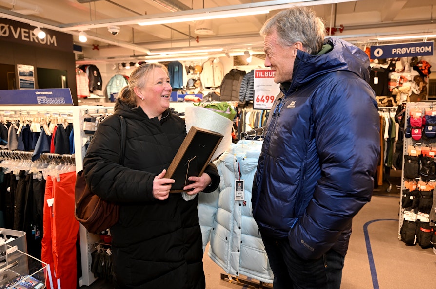 Kretsvinner fra Finnmark til ildsjelprisen, Lise Marianne Johansen overraskes med prisen av Frode Grodås. Inne i sportsbutikk i Tana.