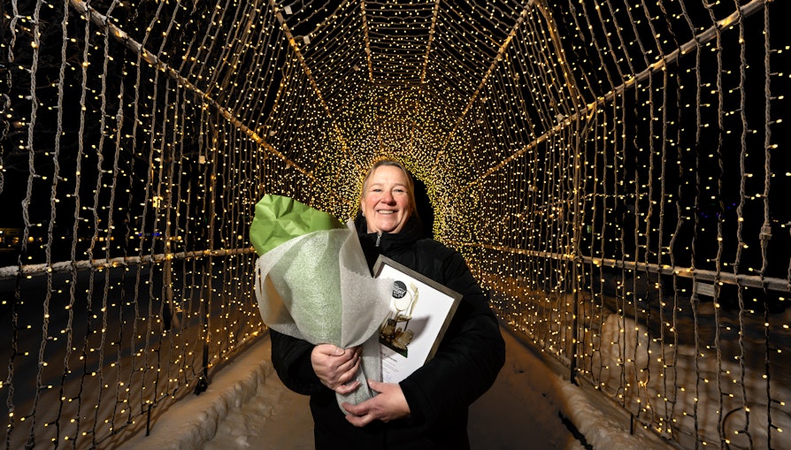 Lise Marianne Johansen står under en lysbue i Tana sentrum. Mørkt rundt. Vinter. Kaldt.