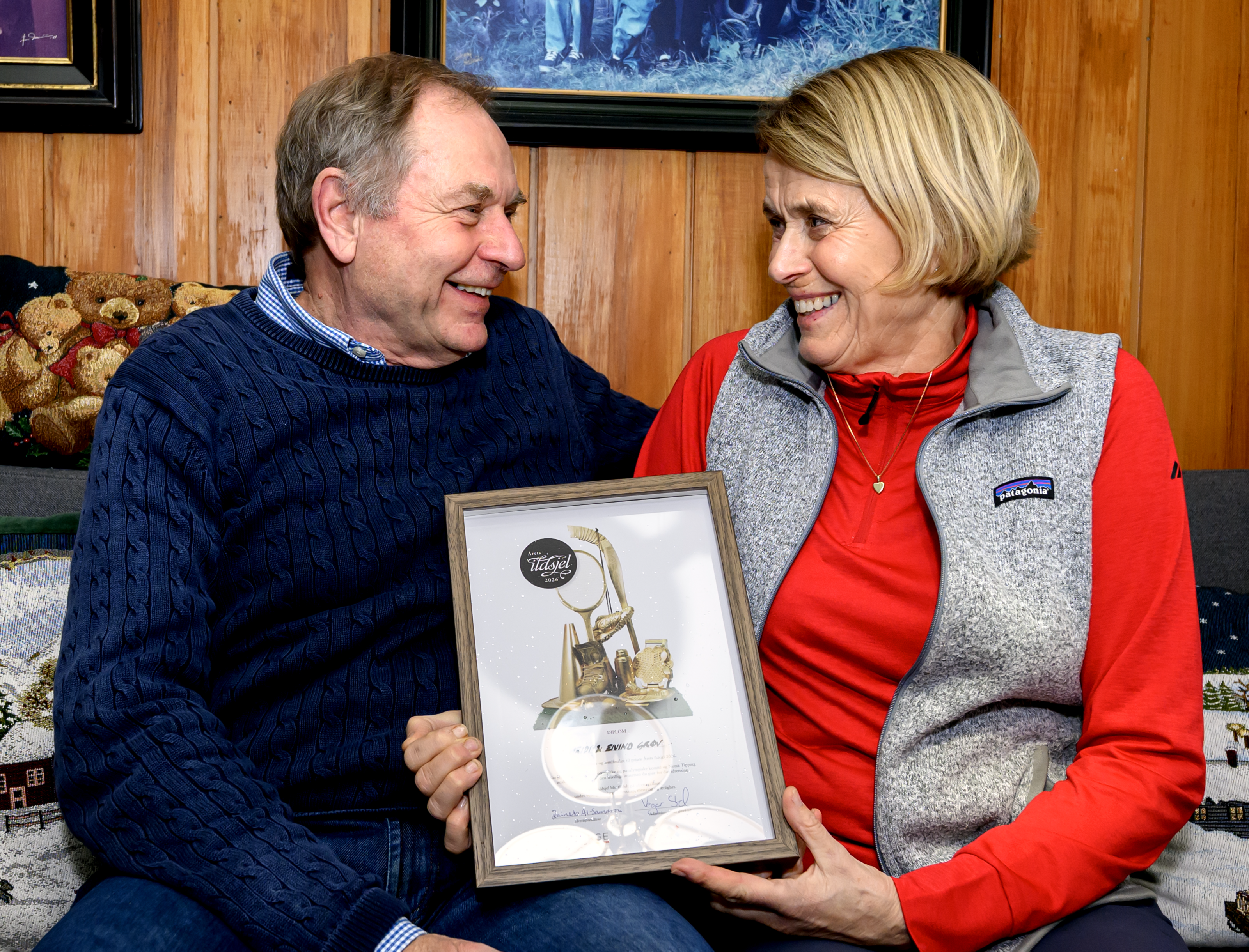 Eivind Grøv og kona Heidi Sørum Grøv (Byaasen Skiklub) er kretsvinnere fra Trøndelag til Ildsjelprisen 2026. Her sitter de sammen i soafen hjemme, med diplomet mellom seg.  Foto: Ola Thorset, Norsk Tipping)