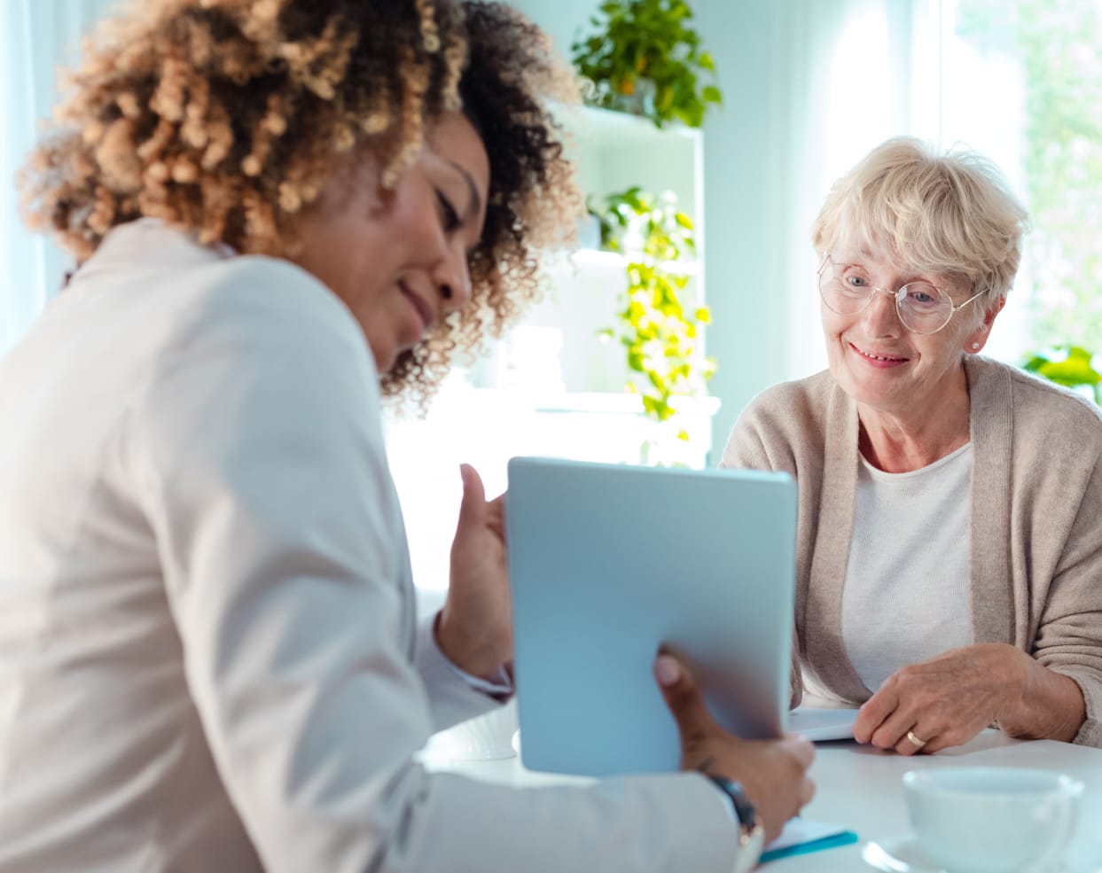 A woman showing an elderly lady an item that looks like a tablet.
