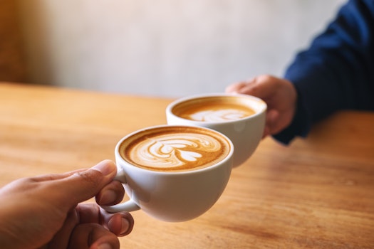 Close-up beeld van een man en een vrouw die twee koffiemokken klinken