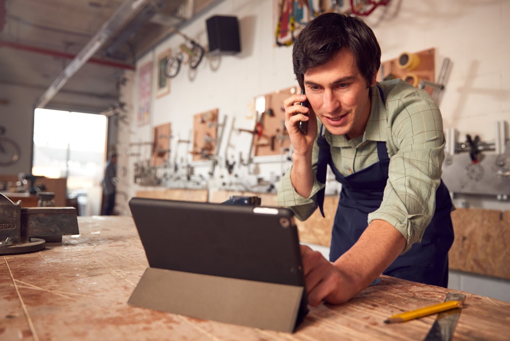 Bedrijfseigenaar in werkplaats die een digitaal tablet gebruikt en belt met een mobiele telefoon