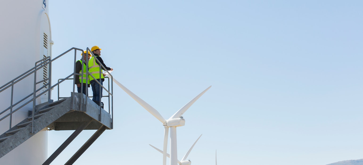 Des ouvriers se tiennent debout sur une éolienne dans un paysage rural
