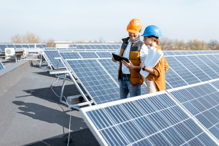 Deux ingénieurs ou architectes explorent la construction d'une centrale solaire, marchant avec une tablette numérique sur un toit.