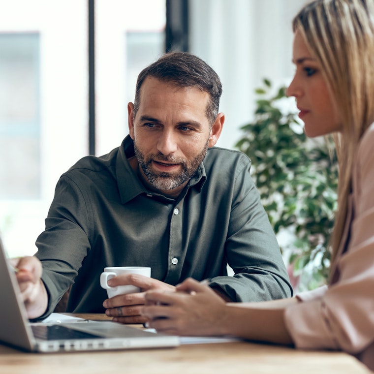 Slimme zakenmensen werken samen met een laptop terwijl ze praten in de coworking plek.