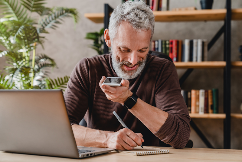 Man met baard belt met telefoon terwijl hij noteert