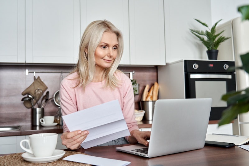 Vrouw kijkt naar laptop met papieren in de hand