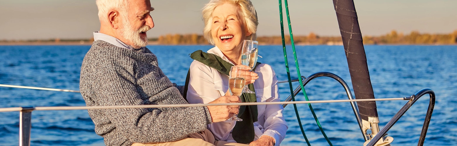 Wealth planning at PIA Group Happy couple drinking champagne and laughing while relaxing on a sailboat or yacht deck.