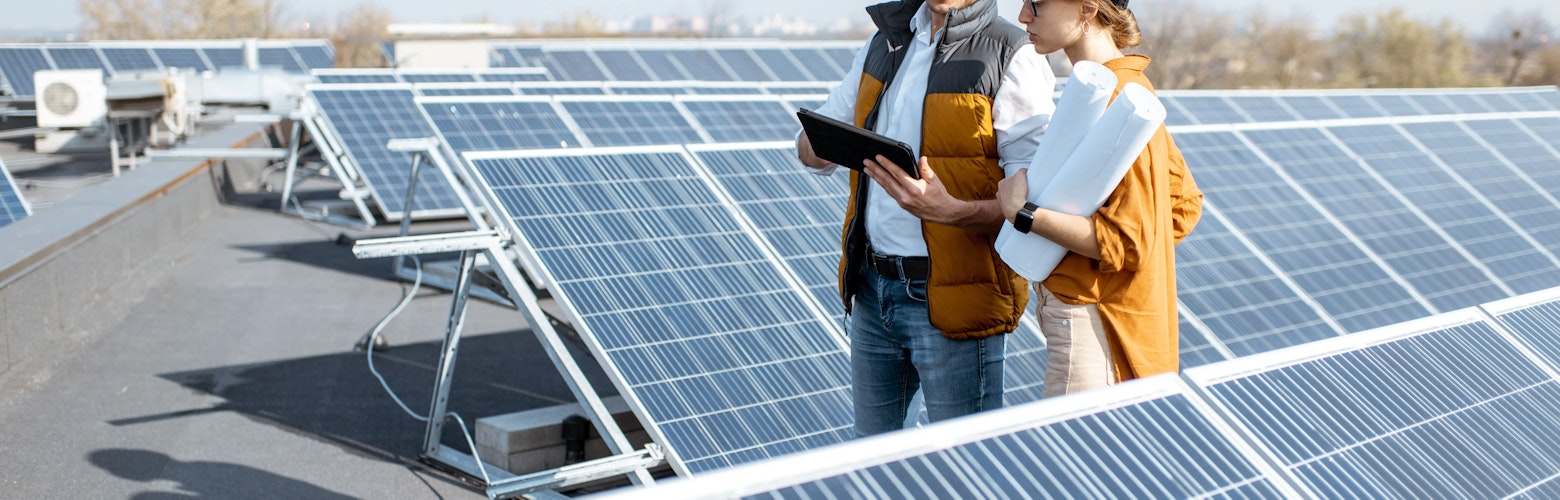 Conseil en investissement chez PIA Group. Deux ingénieurs ou architectes explorent la construction d'une centrale solaire, marchant avec une tablette numérique sur un toit.