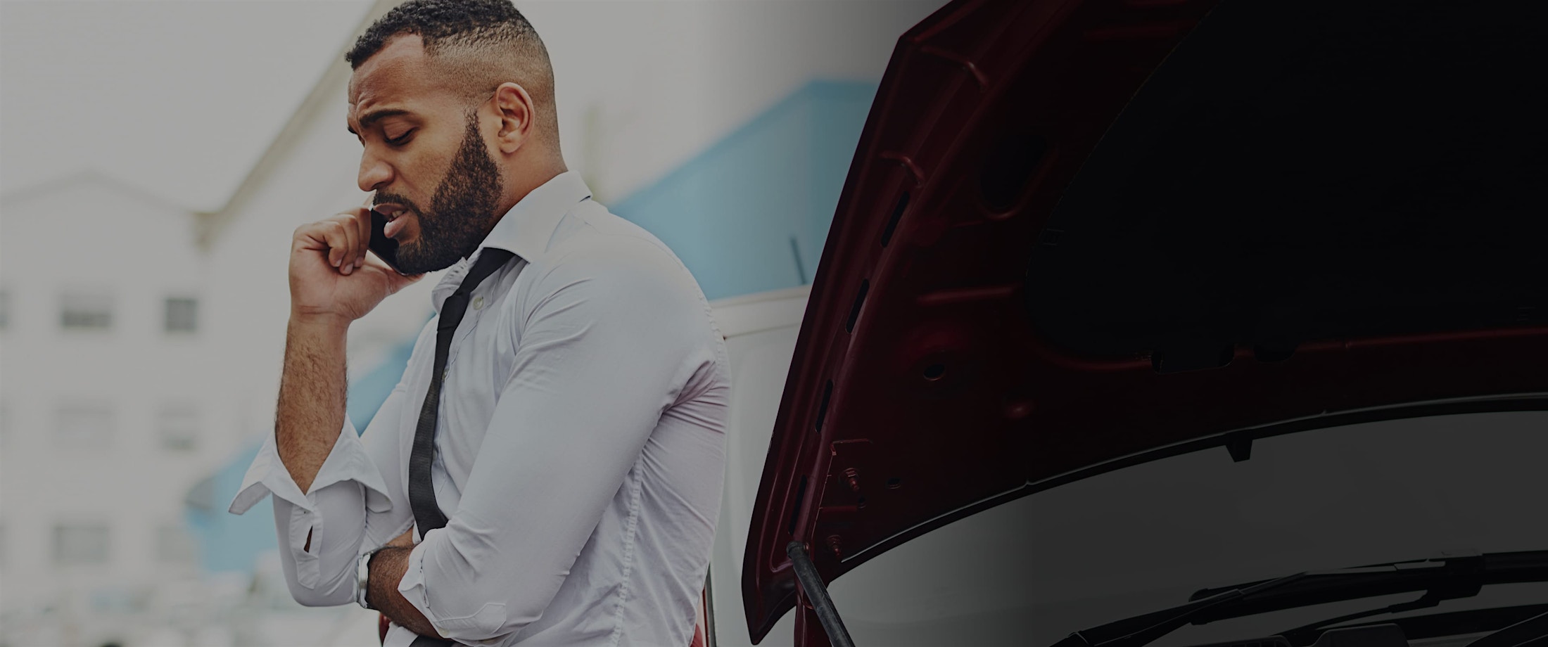 Man in a suit talking on a cell phone next to a wrecked car.