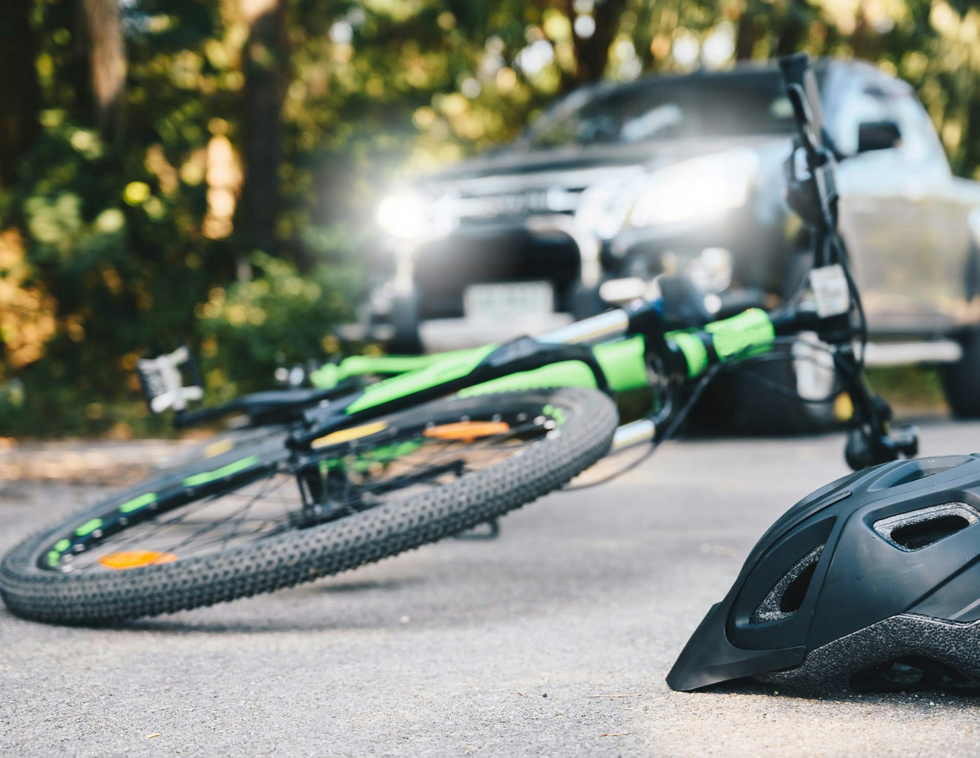 Bicycle and helmet on the ground with a car in the background