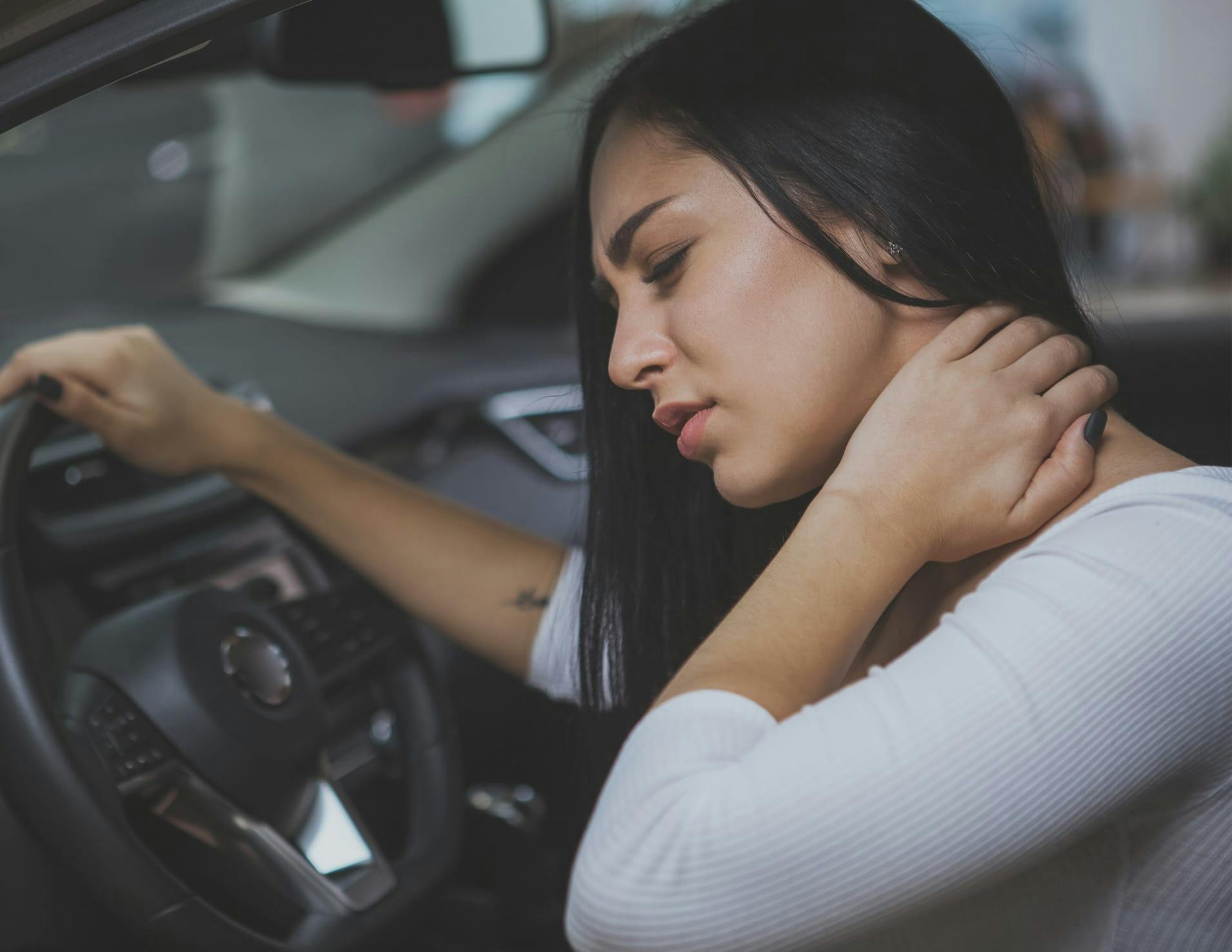 Woman in a car with one hand on her neck