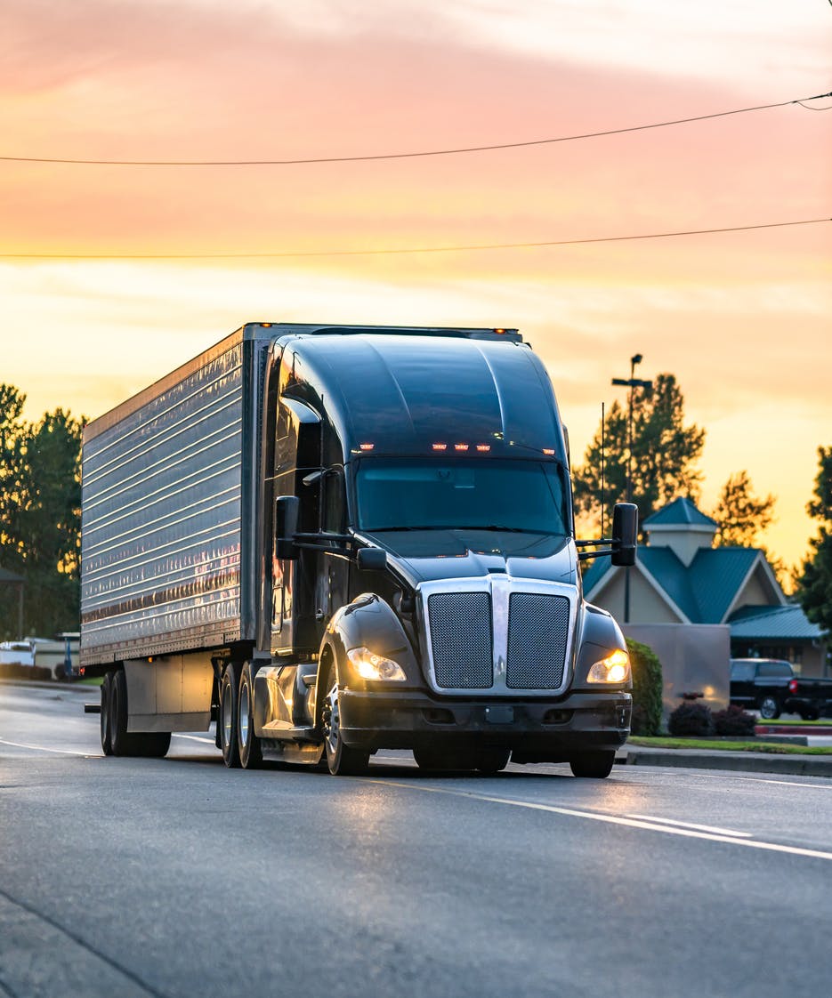 semi truck driving on road at sunset