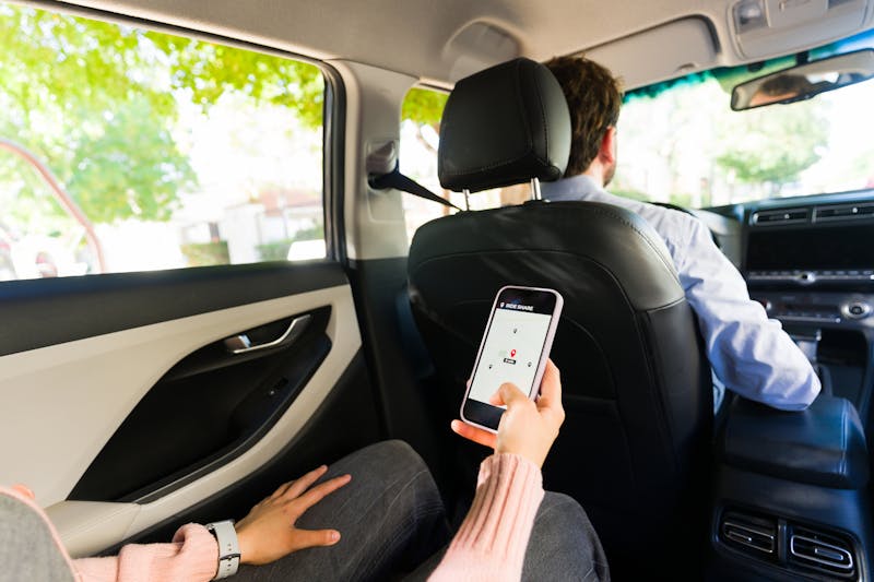 Rideshare passenger using a ride-share app while seated in the back of a vehicle