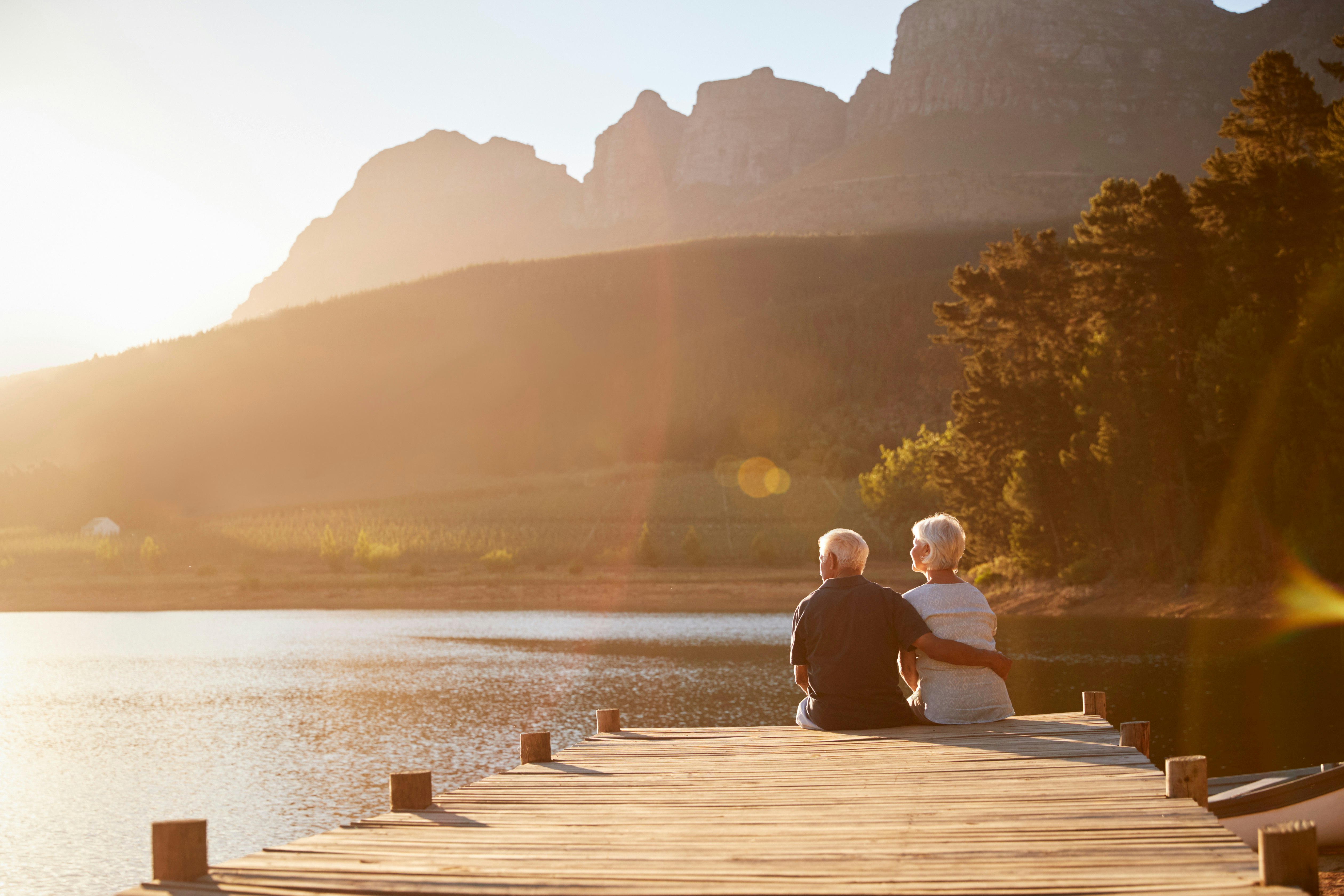A retired couple sits on a dock during sunrise