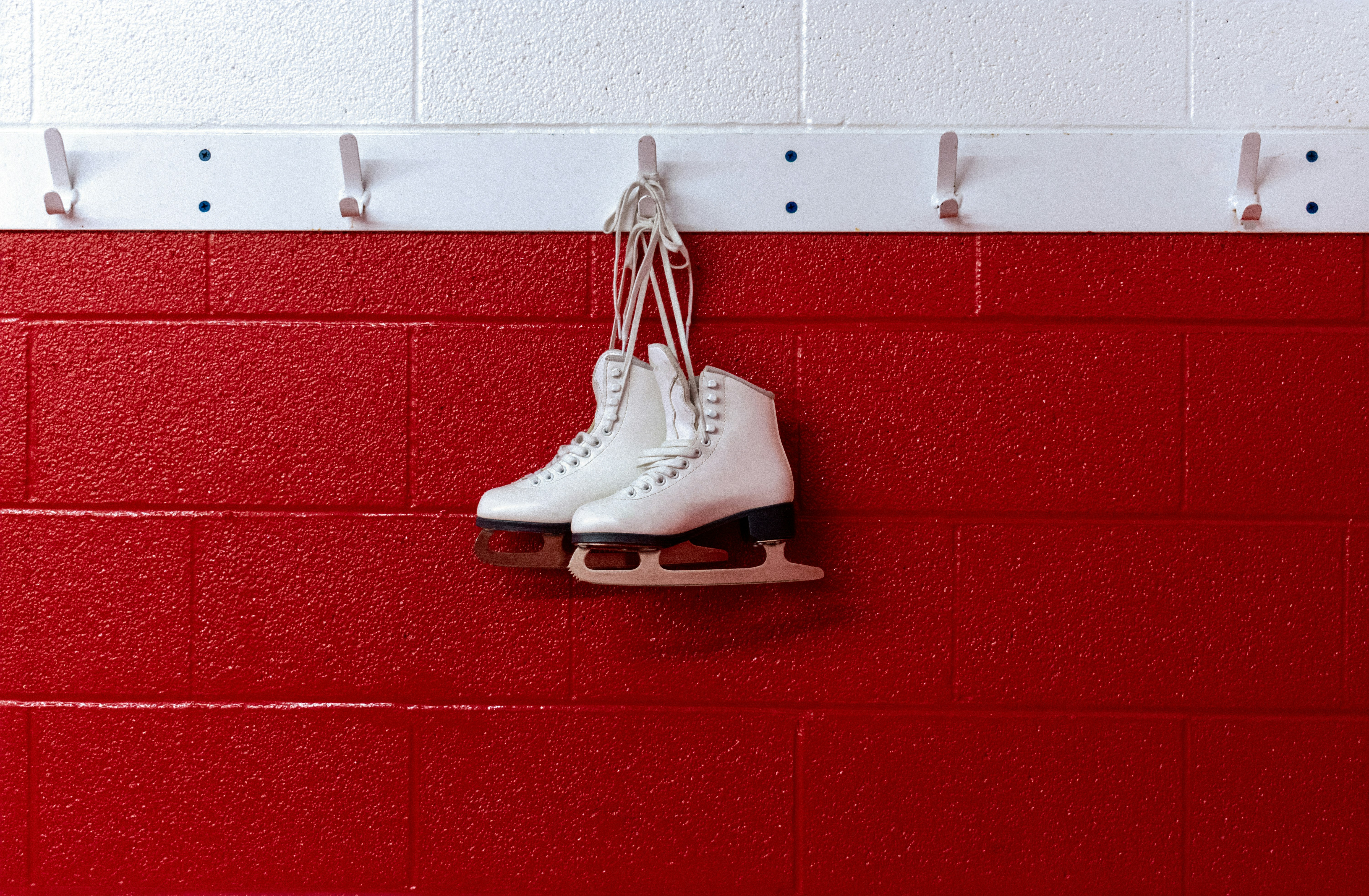 Figure skates hanging in locker room over red background.