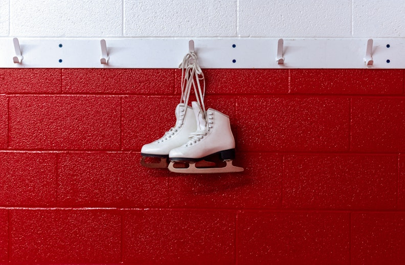 Figure skates hanging in locker room over red background.