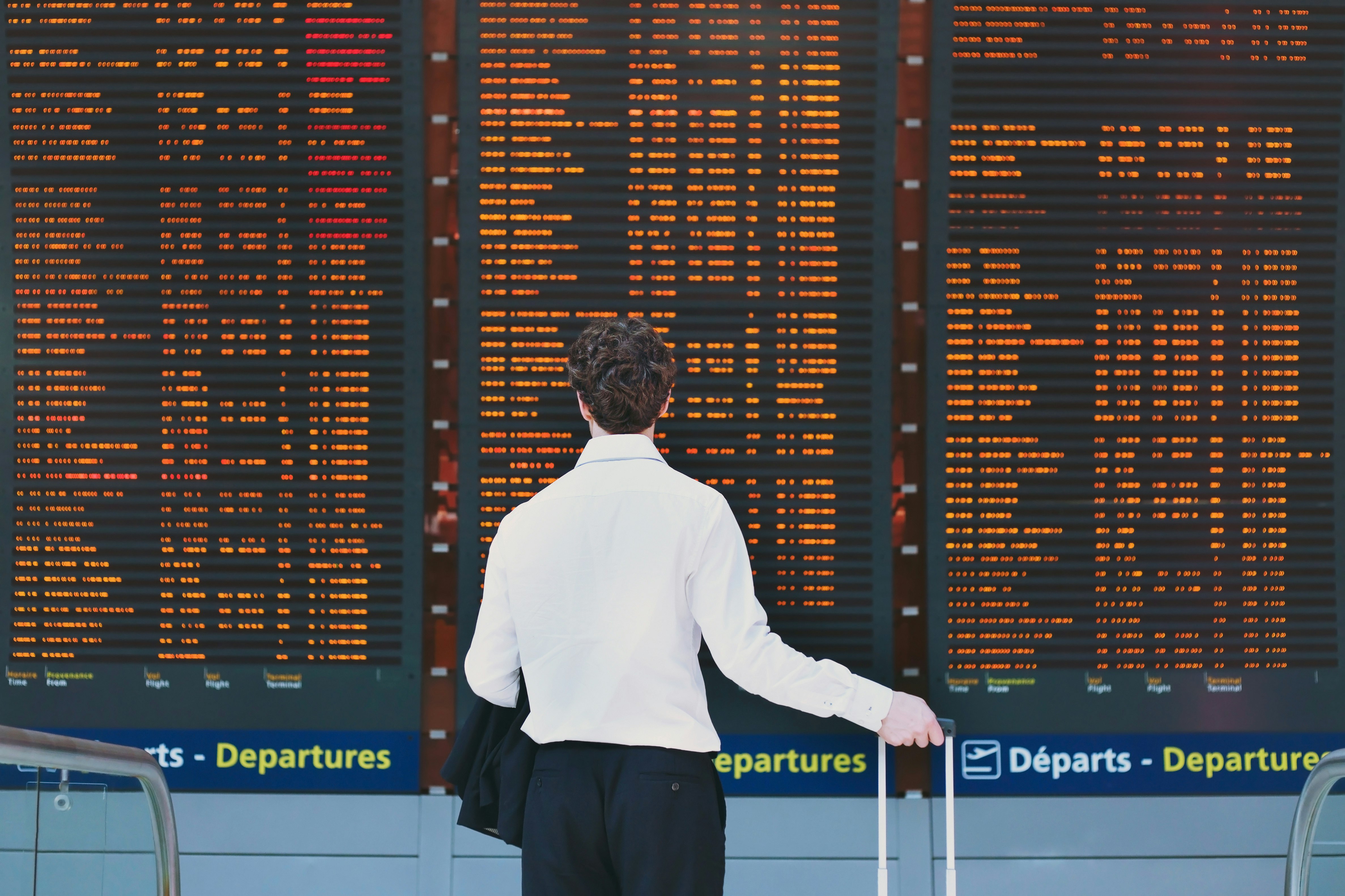 Man in suit looking at flight departures board.