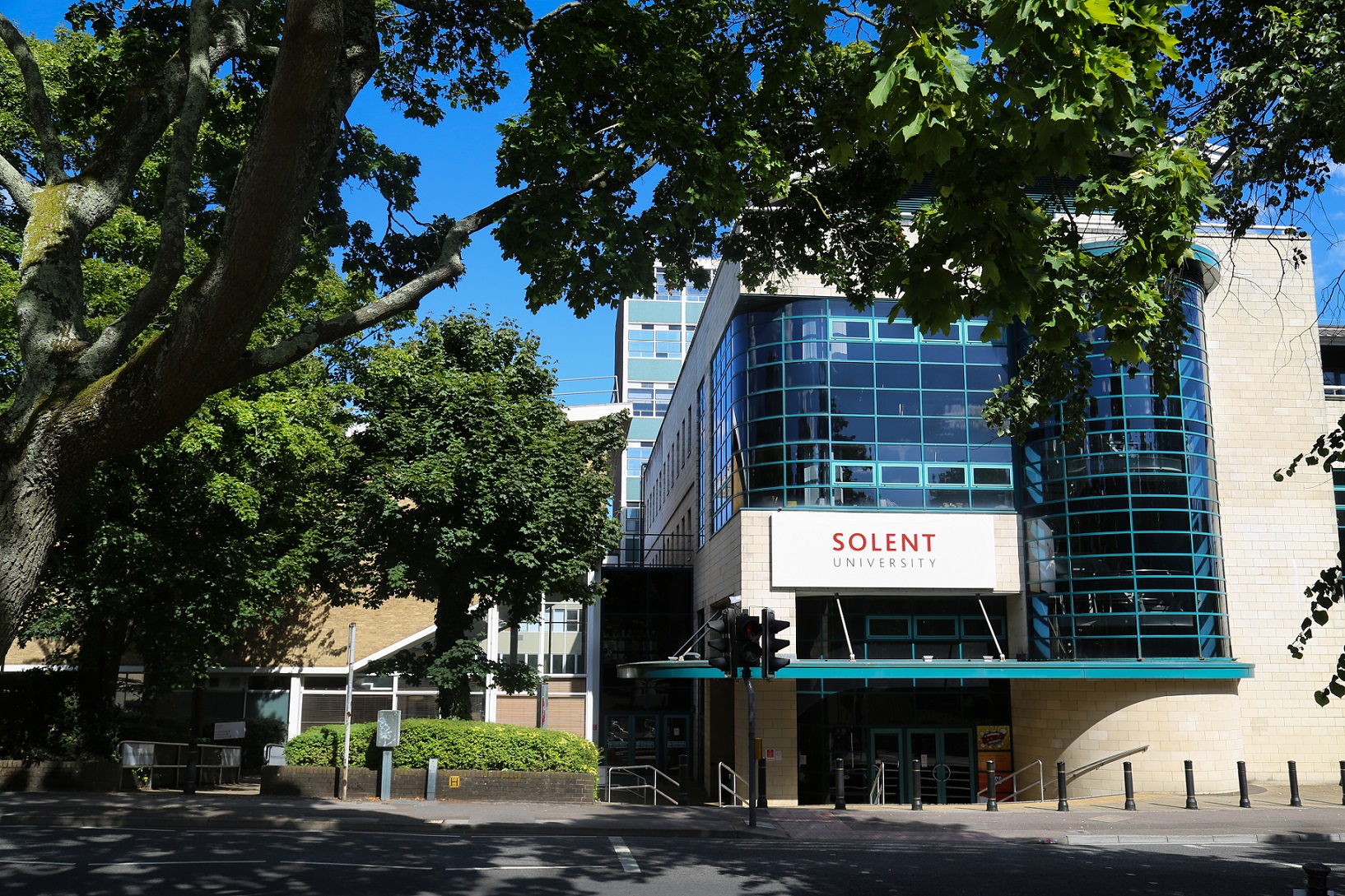 A glass and stone building with the word Solent University on. Sits in amongst trees.