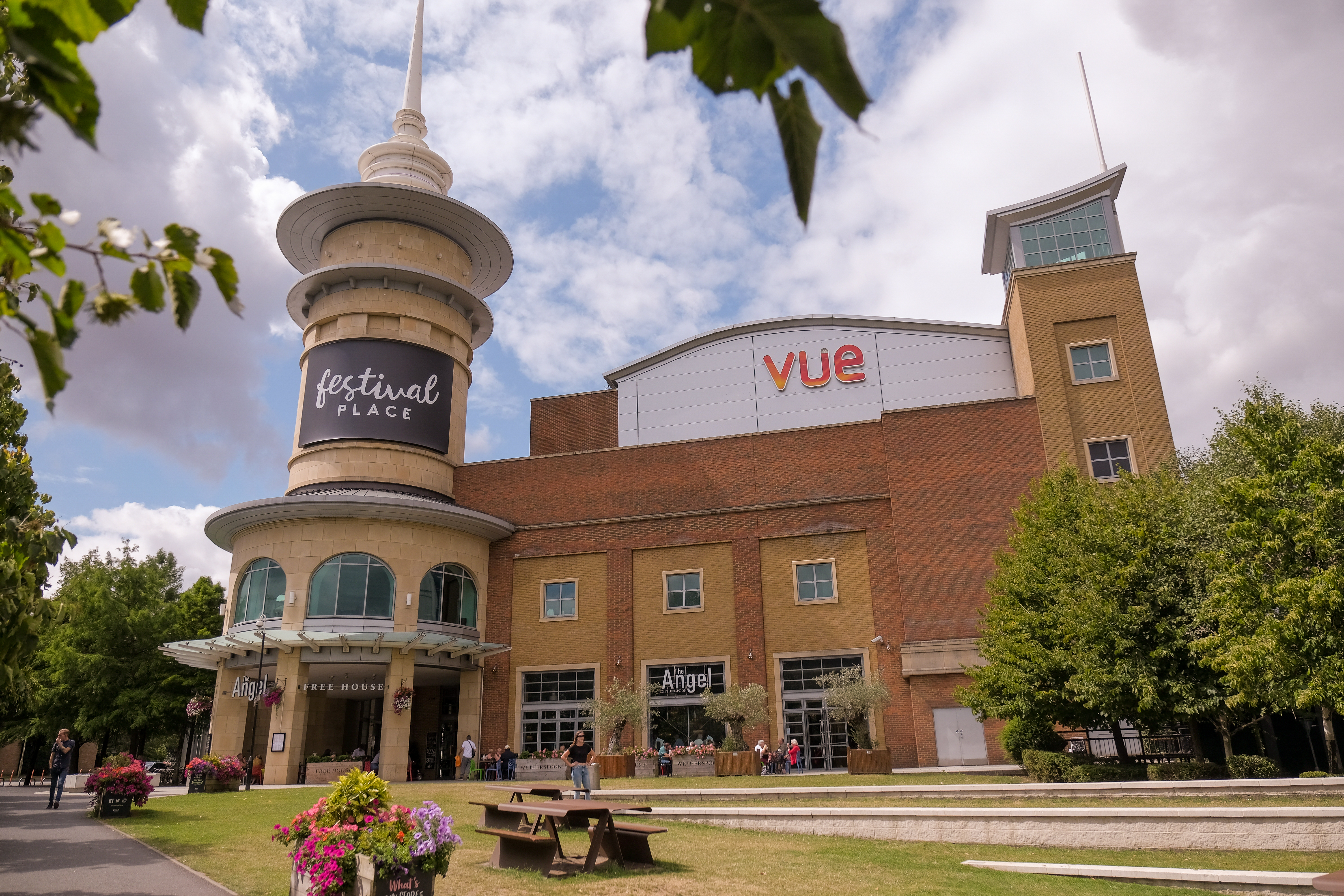 The brick building houses Vue Cinema, The Angel pub and has a turret for Festival Place. Outside you can see a small part of the amphitheatre and some benches.