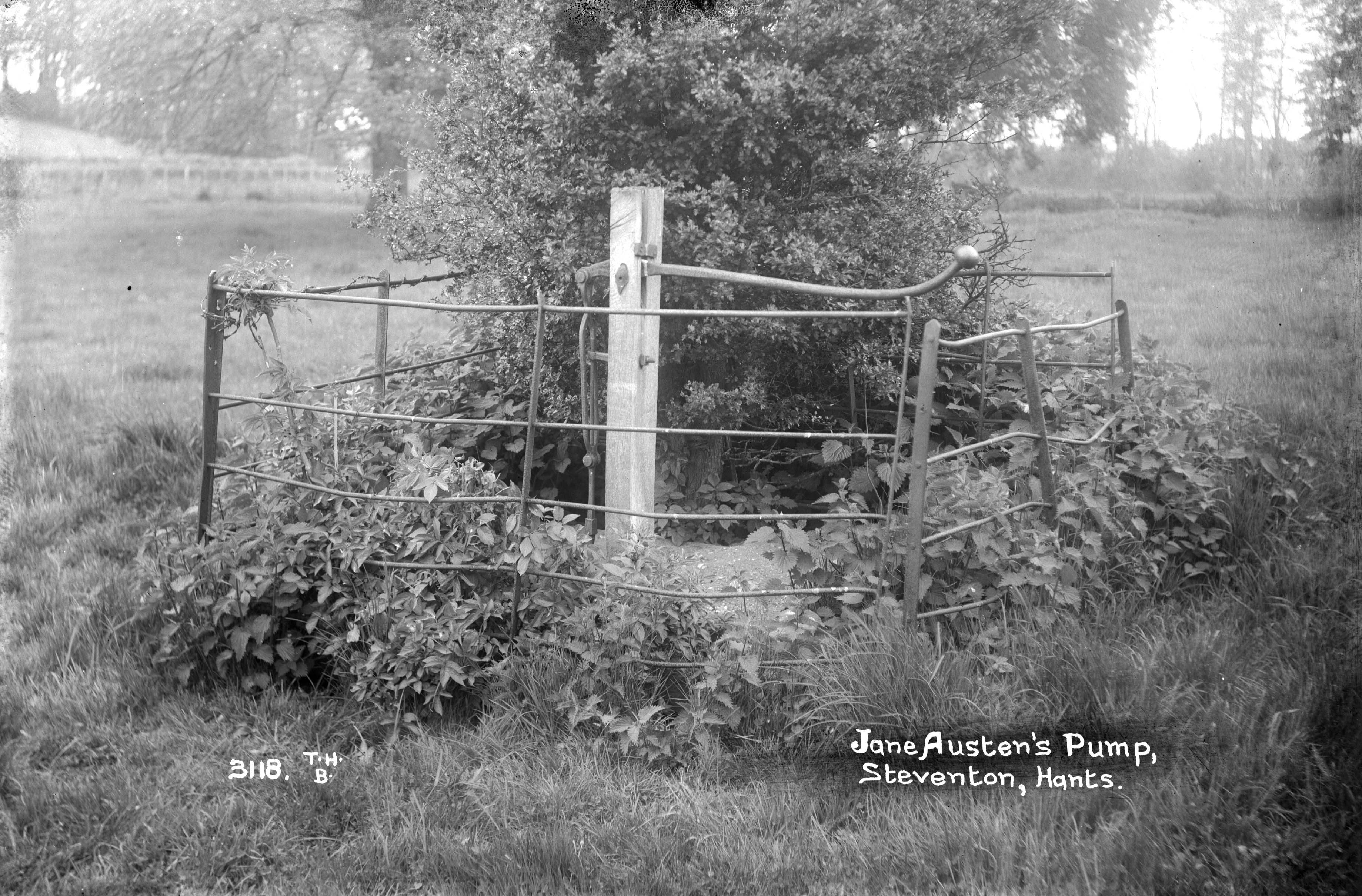 A black and white image. A pump is surrounded by a metal fence.
