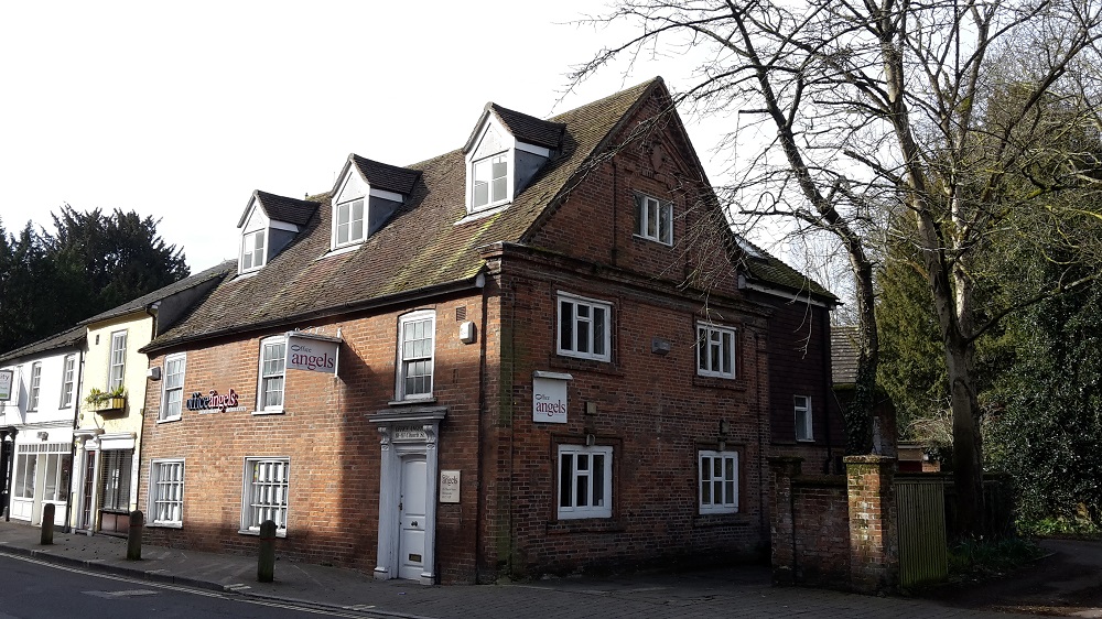 a two storey red brick house with white windows and door. There are dormer windows in the roof. It is attached to some white buildings.