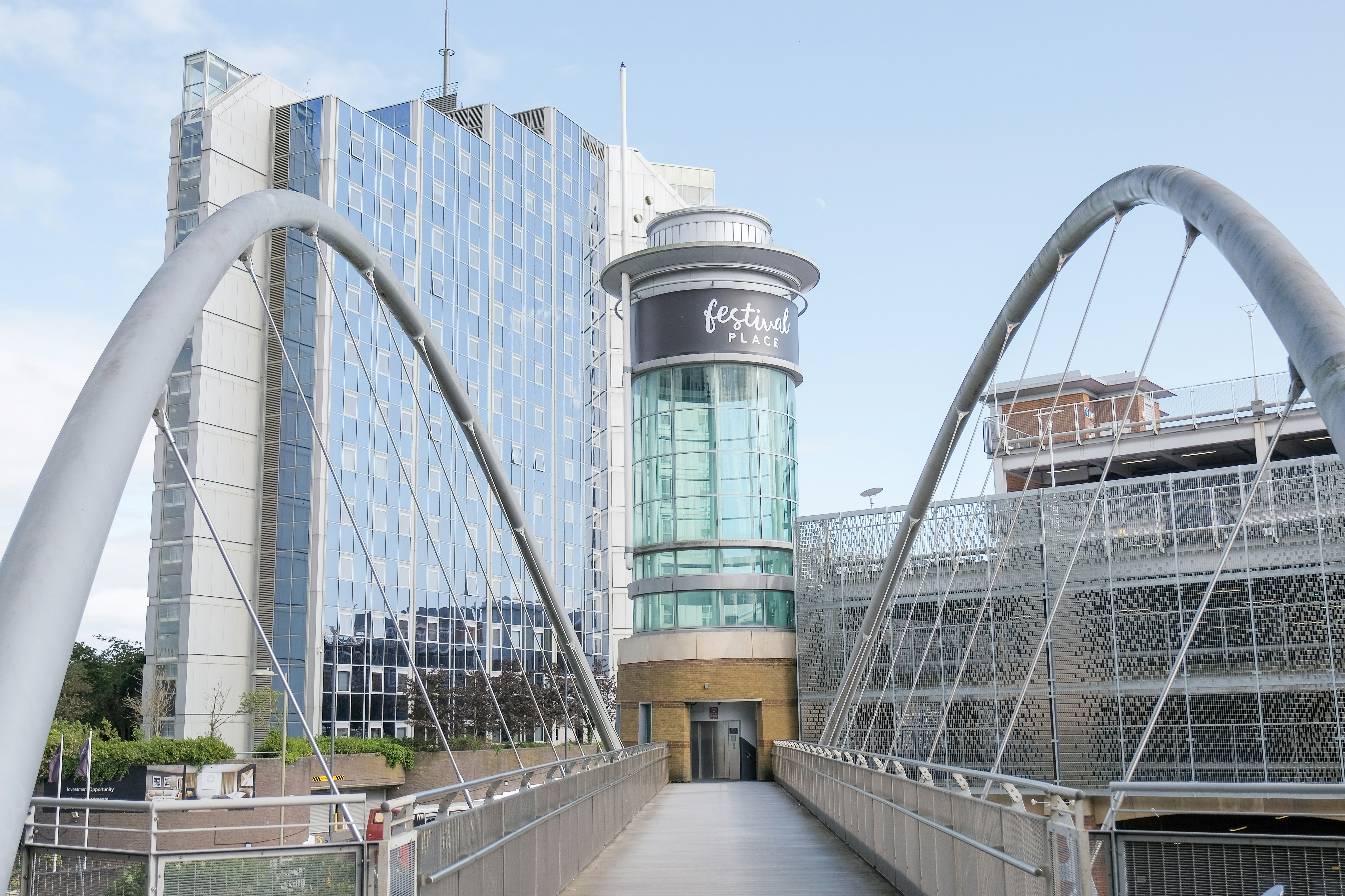 A bridge with Festival Place tower at the end. In the background is an office block and the car park