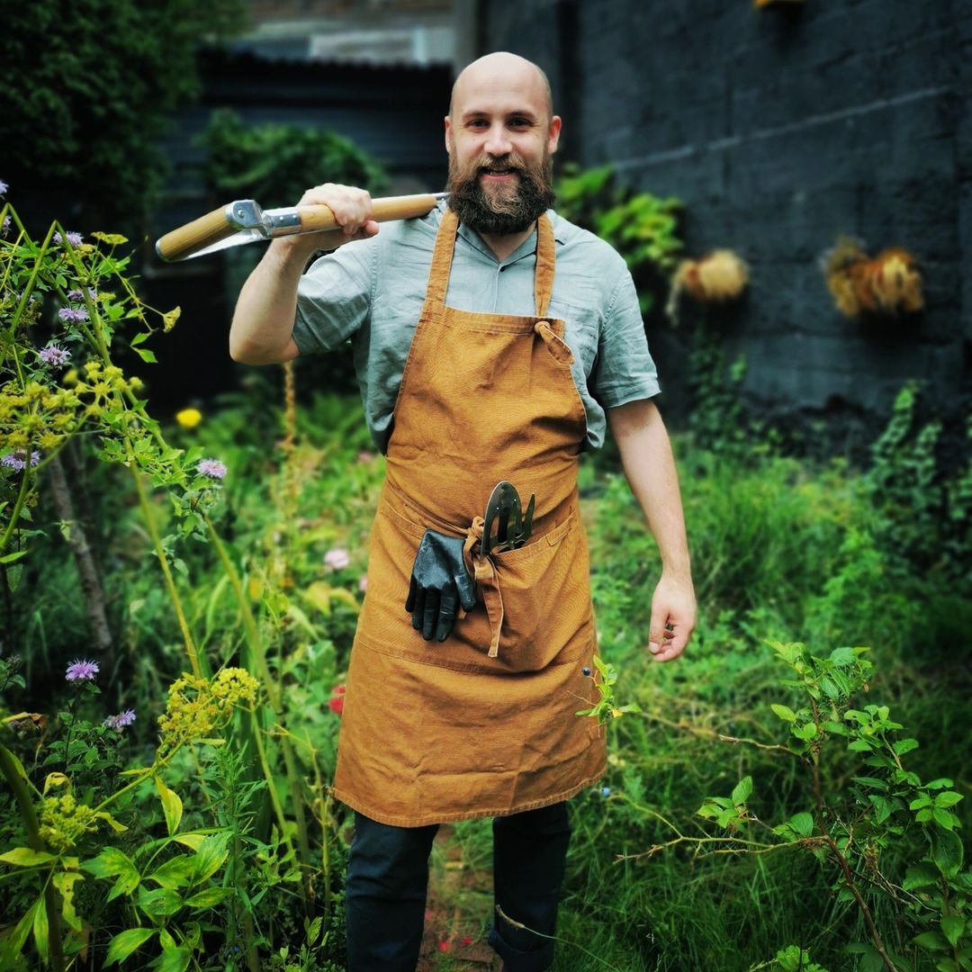 The Beardy Gardener in action, wearing a brown apron which holds tools for planting