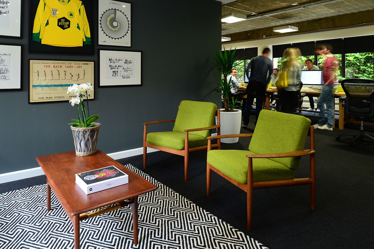 Two lime green chairs sit infront of a table that's on a geometric designed rug. In the background you can see some people