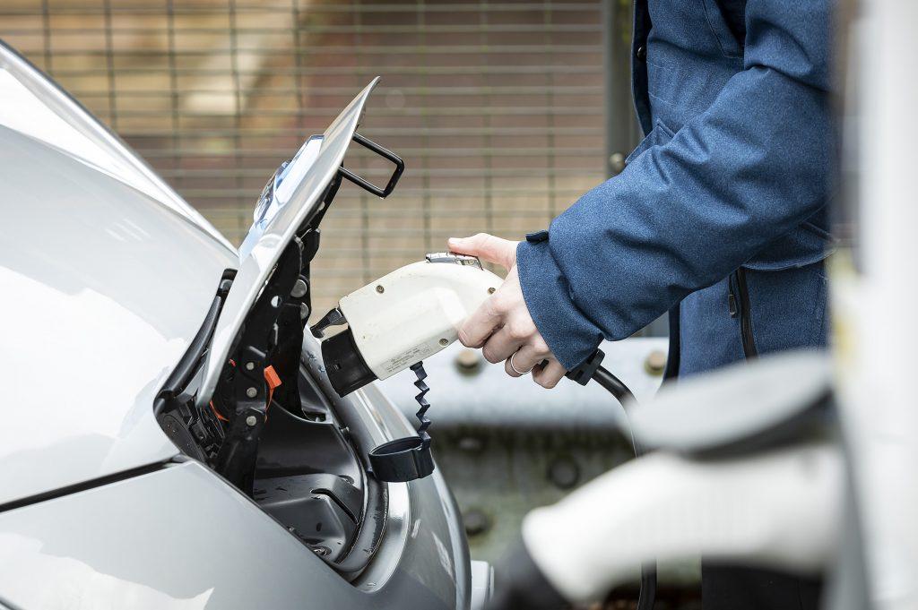 a person holds a electric charging cable and is about to plug it into a car