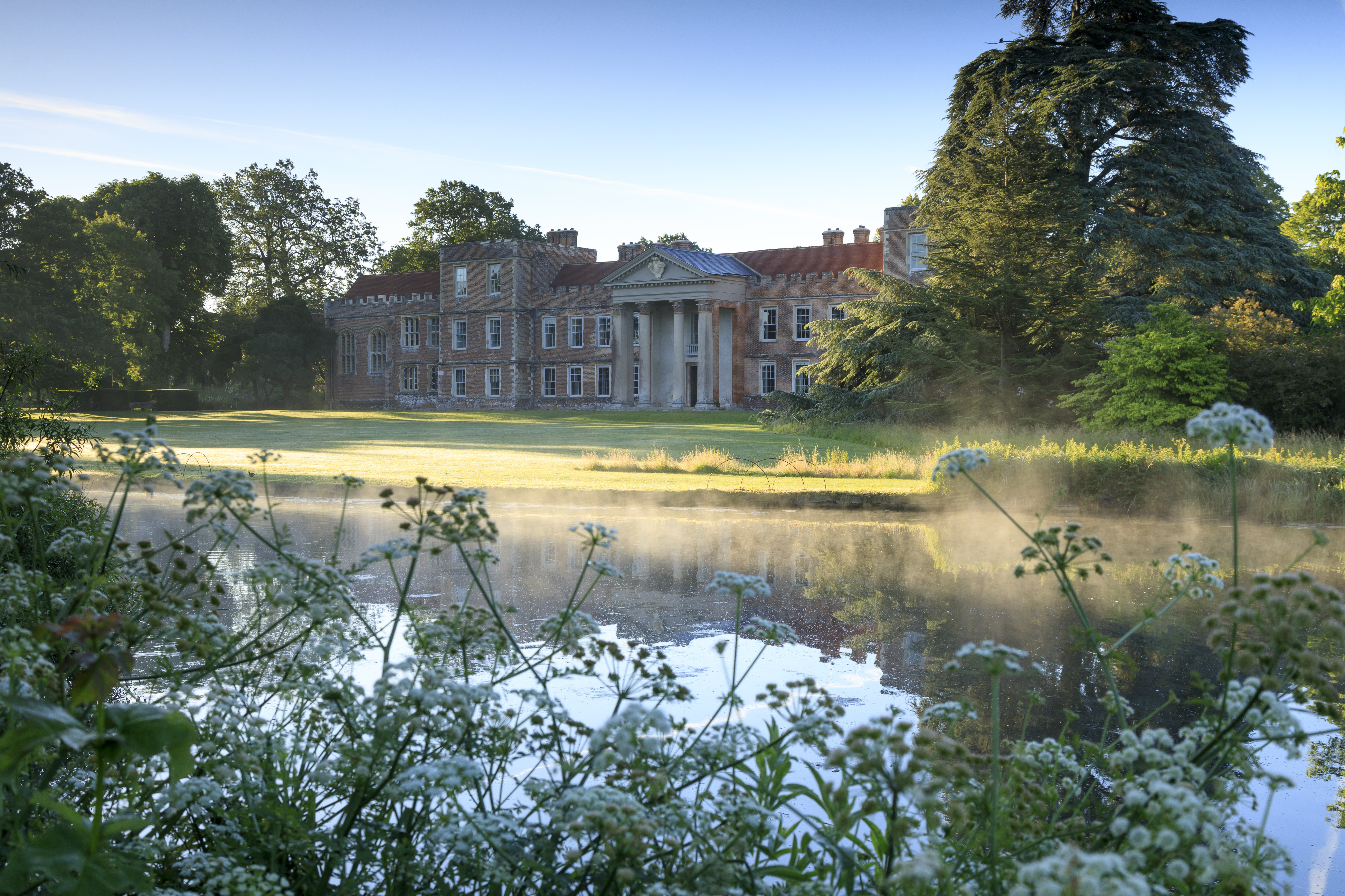 View of the north front across the lake in early morning light at the Vyne, Hampshire. The Vyne is a warm red-bricked Tudor mansion built in the 16th century for Lord Sandys, Henry VIII's Lord Chamberlain, which later passed into the hands of the Chute family, who cared for the house and estate for over 300 years. It was remodelled to its present configuration in the mid-17th century.