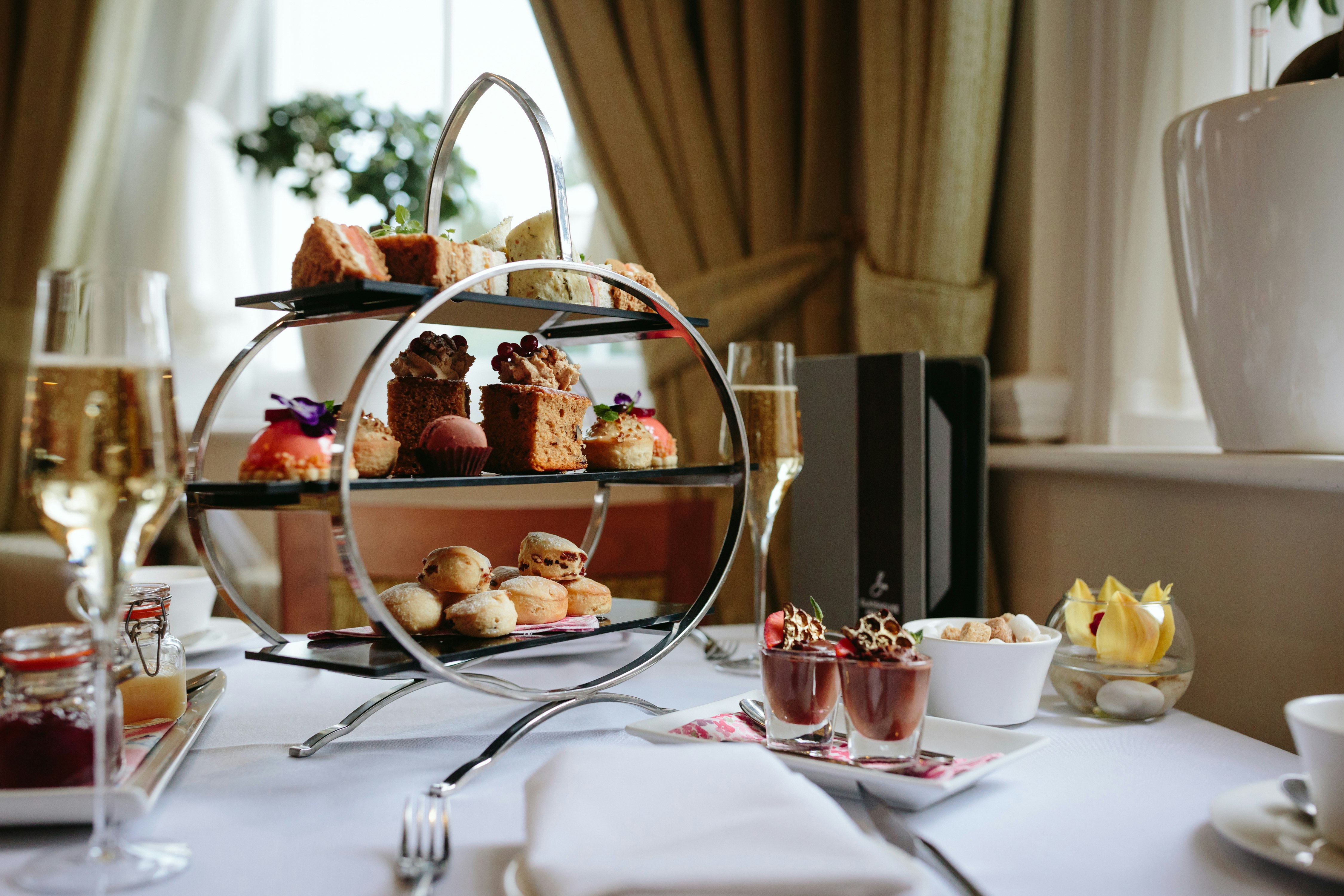 A cake stand filled with cakes, scones and strawberries. Two glasses of fizz.