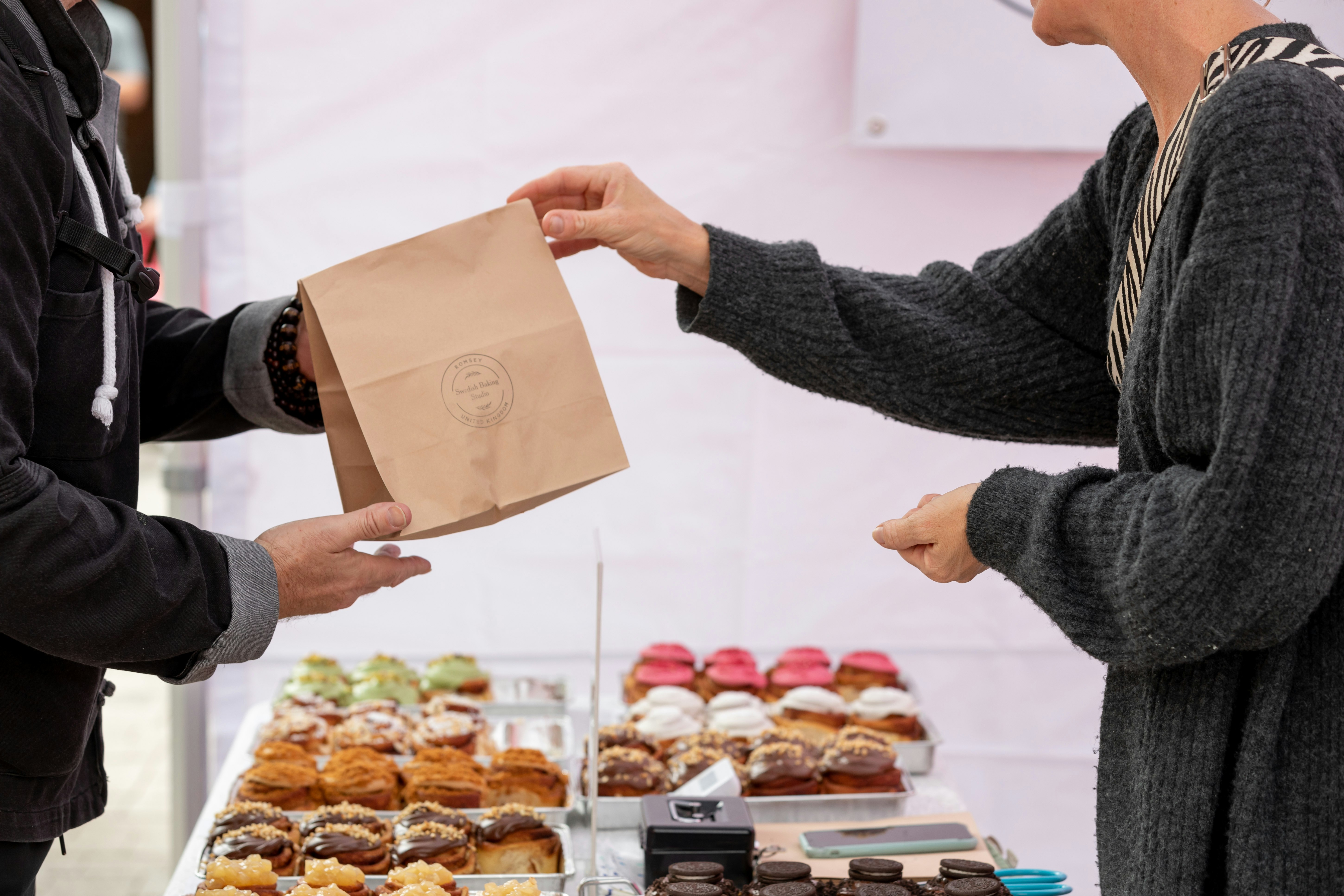 A person hands over a paper bag. Beneath are baked goods.