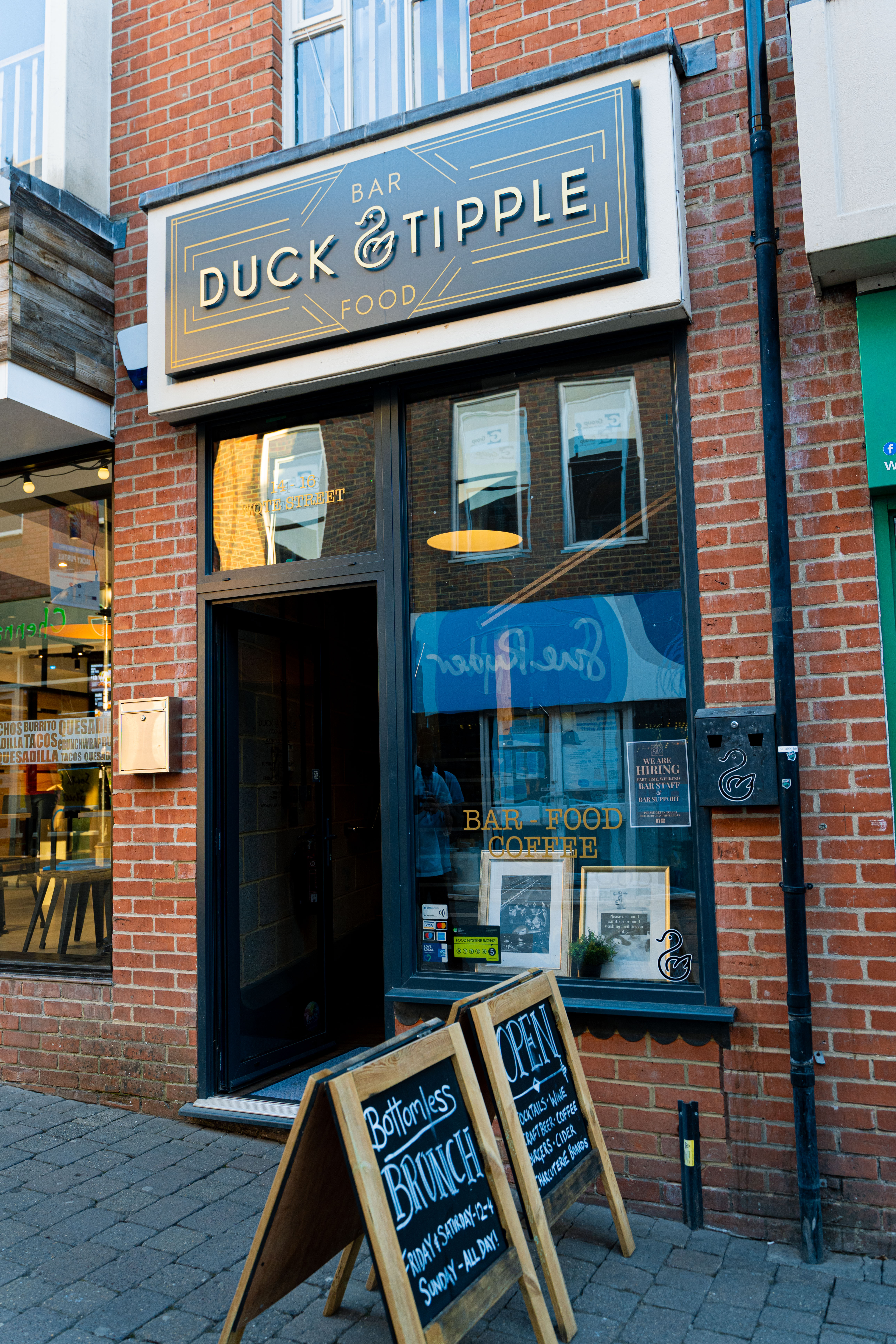 The outside of the Duck and Tipple bar. You can see two sign boards outside, one says Open and the other promotes the bottomless brunch.