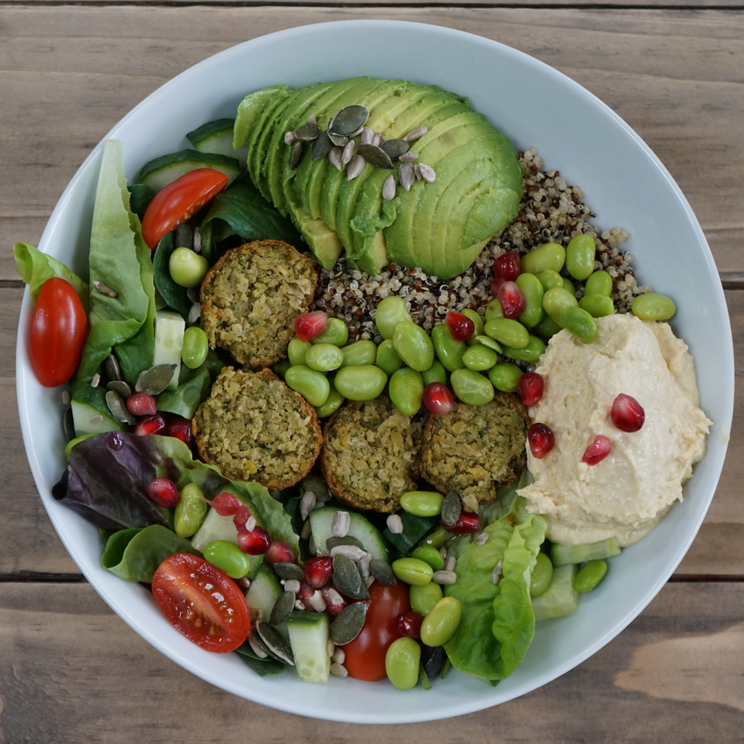 A rainbow of colourful food within a white bowl. Ingredients include tomatos, lettuce, avocado and edamame beans.